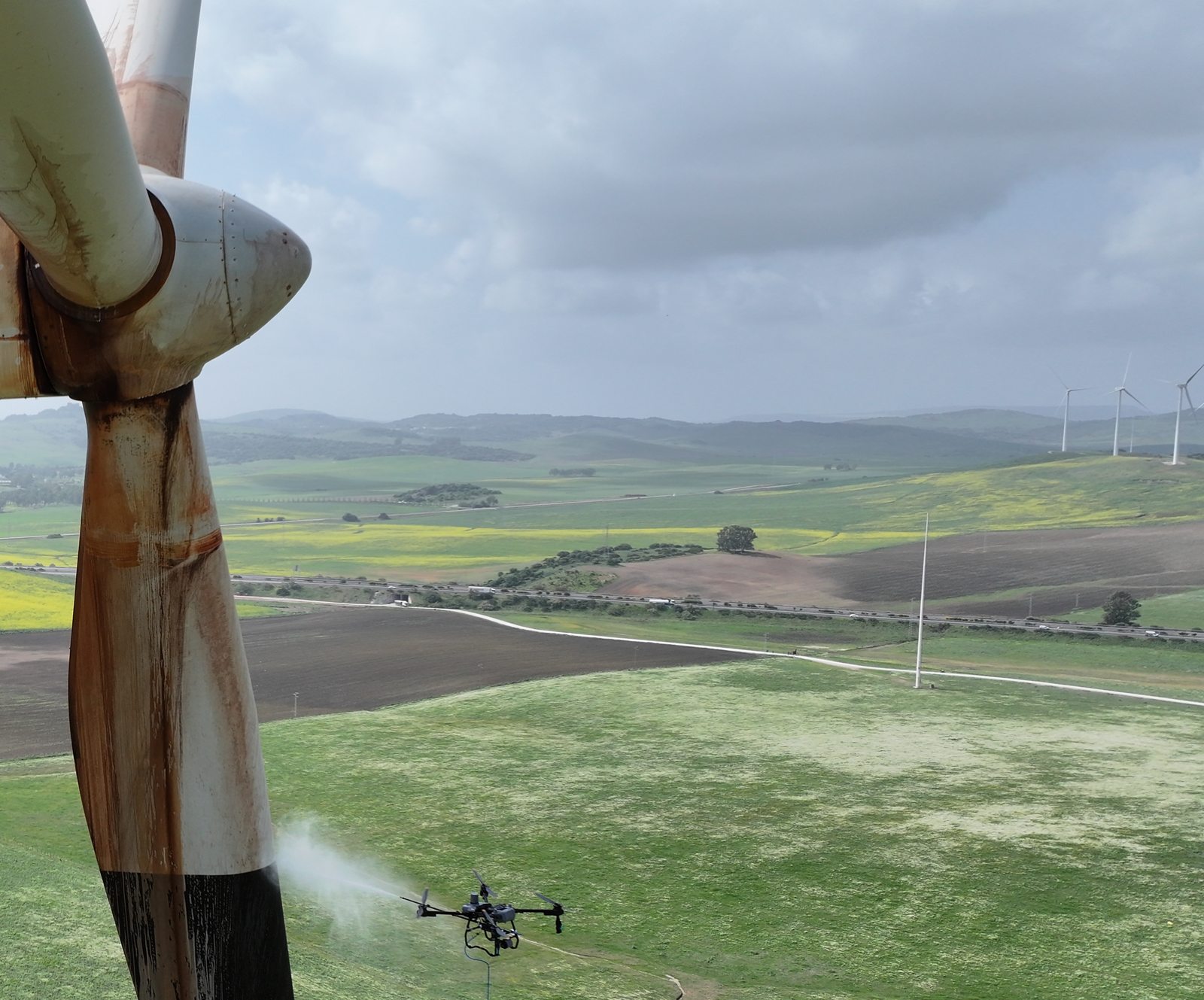 Dron limpiando la pala de un aerogenerador con agua a presión, en vuelo