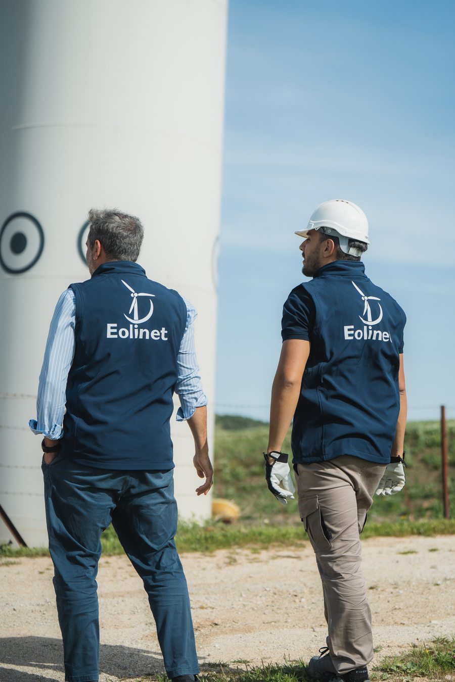 Dos técnicos de Eolinet caminando junto a la torre de un aerogenerador